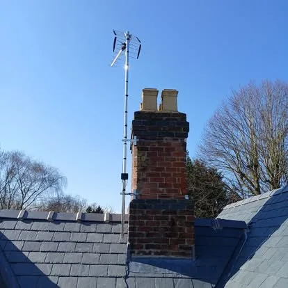 An aerial mounted to a brick chimney stack against a clear sky, slate roofs below.