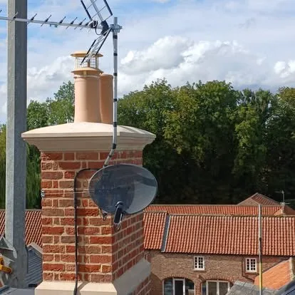 A dish and aerial on a chimney stack, rooftops running away behind.