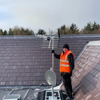 An engineer in hi-vis on a slate roof, beside a newly fitted and aligned aerial.